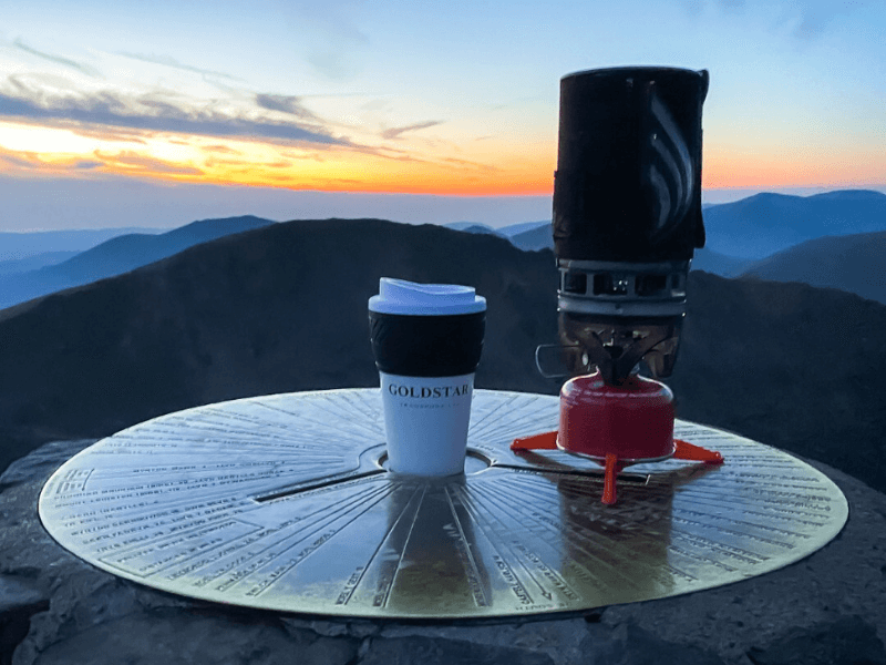 Goldstar travel mug and coffee Jetboil resting on top of Eryri Snowdon mountain toposcope at sunrise with a view of the surrounding peaks